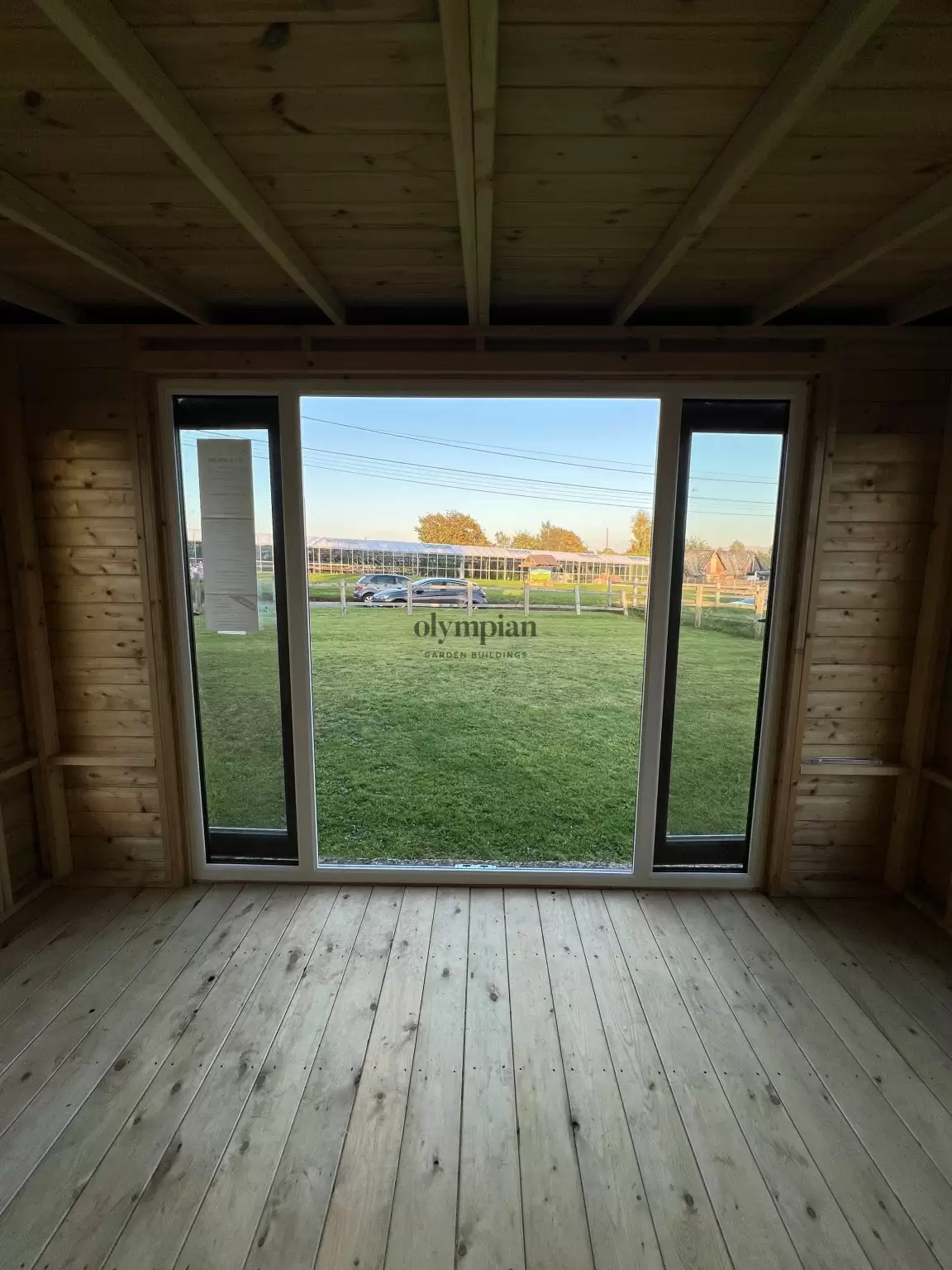Interior view looking out of a 12ft x 8ft garden building with single-sloping roof and UPVC doors, into an open field setting
