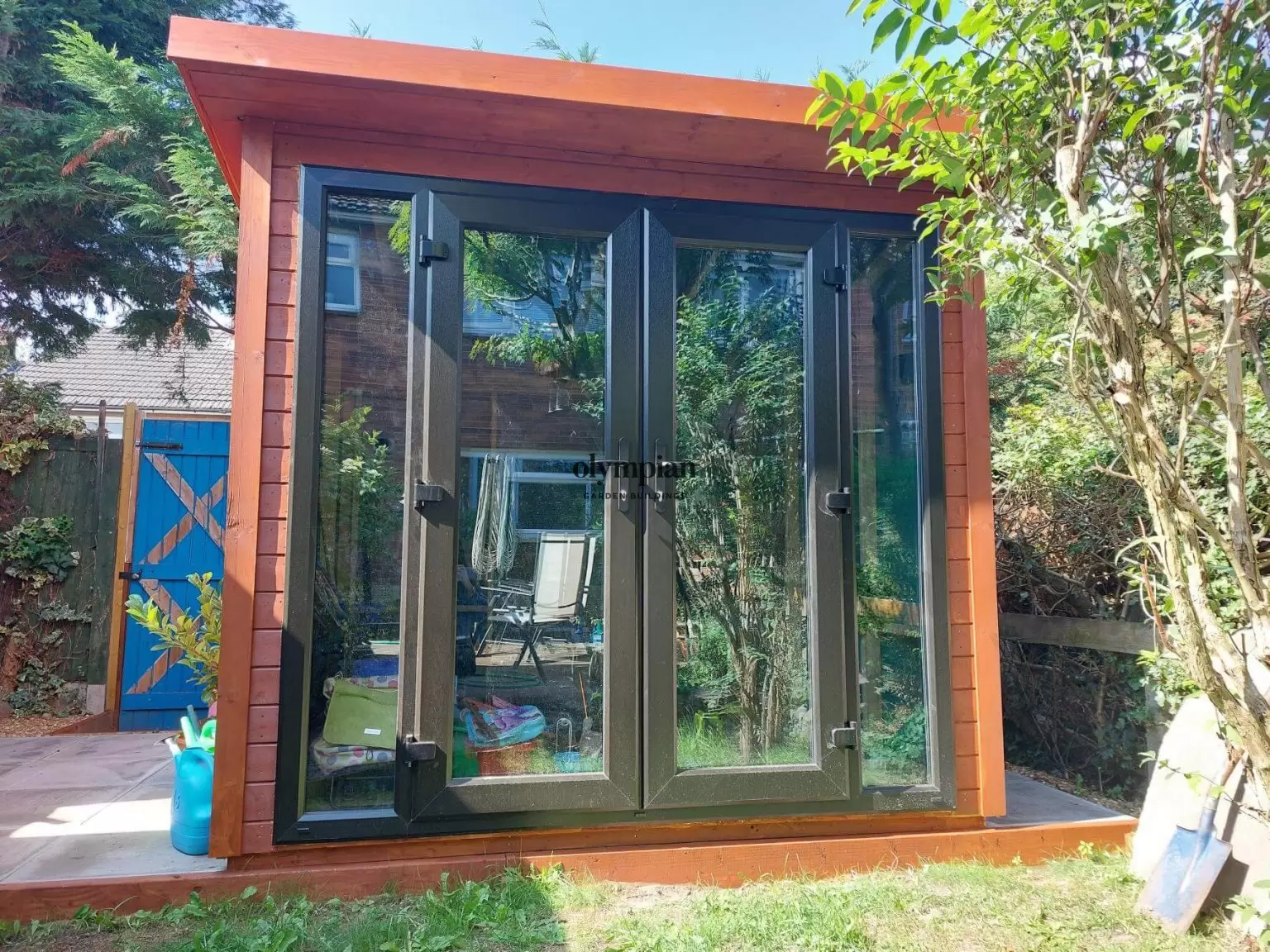 An 8ft x 8ft garden building with single-sloping roof and UPVC doors in the corner of a garden